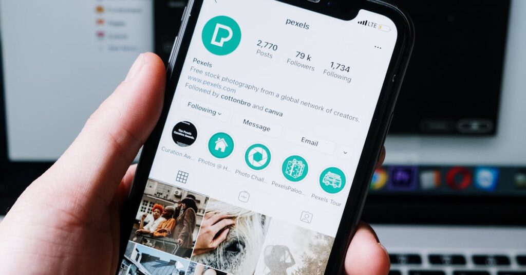 Hand holding smartphone displaying social media app with laptop in the background.